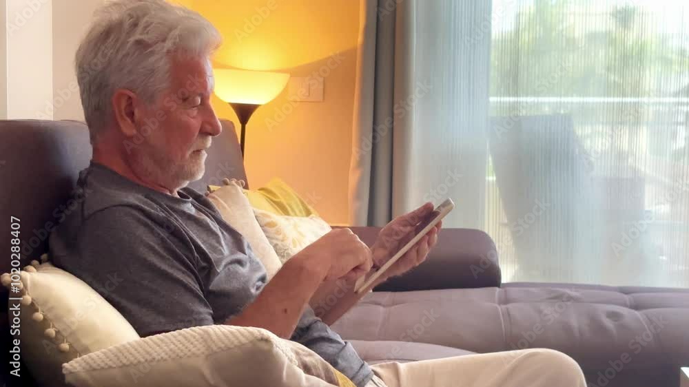Senior man comfortably navigating the internet from his home couch, searching for information, sending emails, and staying up-to-date with social media. Elderly people adapting to modern technology Senior man comfortably navigating the internet from his home couch, searching for information, sending emails, and staying up-to-date with social media. Elderly people adapting to modern technology