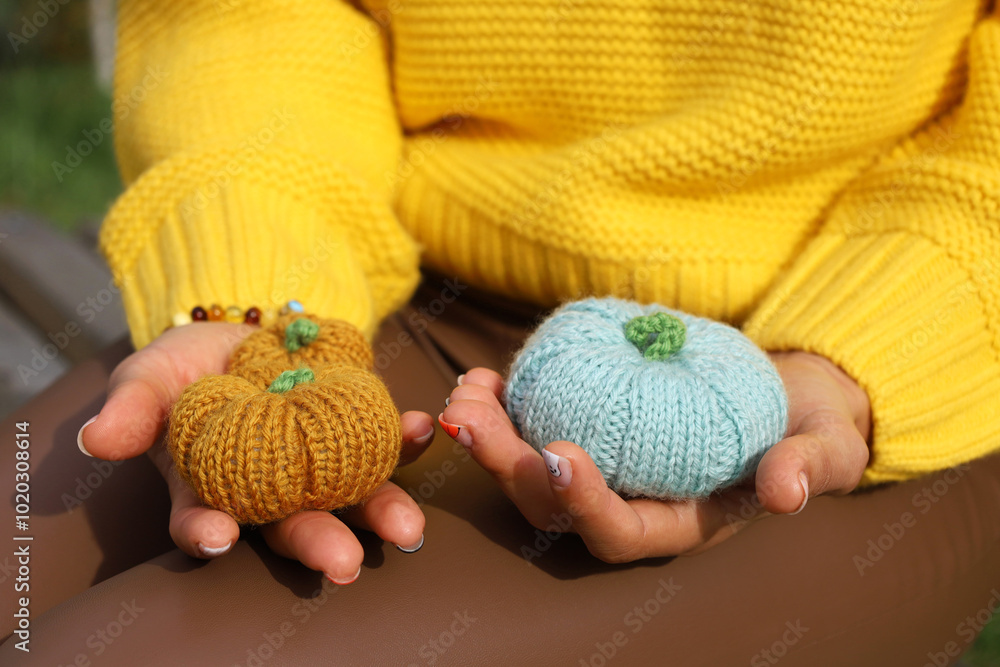 Handmade knitting pumpkins orange and blue in woman's hands, no face, unrecognizable. Close up. Person wearing yellow sweater and brown leather pants. Fall autumn concept.