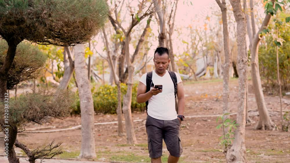 Asian man tourist calling on smartphone. Young hiker walking in forest camp, using mobile phone, traveling and hiking alone. Summer tourism, wild nature. Asian man tourist calling on smartphone. Young hiker walking in forest camp, using mobile phone, traveling and hiking alone. Summer tourism, wild nature.