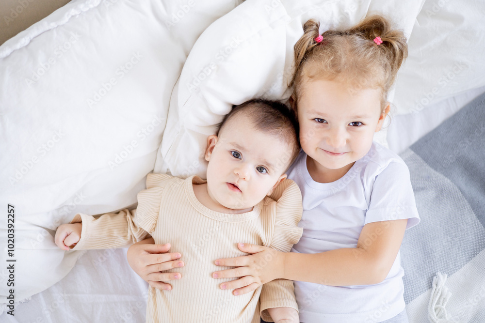 two sisters' children cuddle on the bed at home, the older sister holds the baby at home on the bed, the sisters' love and friendship in the family two sisters' children cuddle on the bed at home, the older sister holds the baby at home on the bed, the sisters' love and friendship in the family