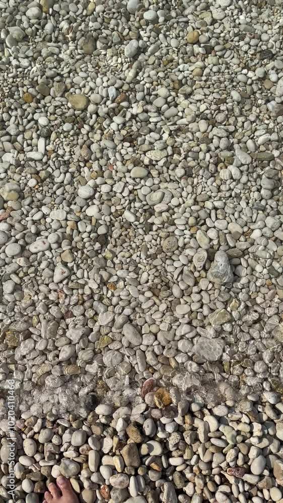 CLOSEUP, TOP TO DOWN: A calming view of sea water flowing gently over a pebble beach. A calm and meditative summer scene from the Adriatic beach as the crystal clear sea flows over the white rocks. CLOSEUP, TOP TO DOWN: A calming view of sea water flowing gently over a pebble beach. A calm and meditative summer scene from the Adriatic beach as the crystal clear sea flows over the white rocks.