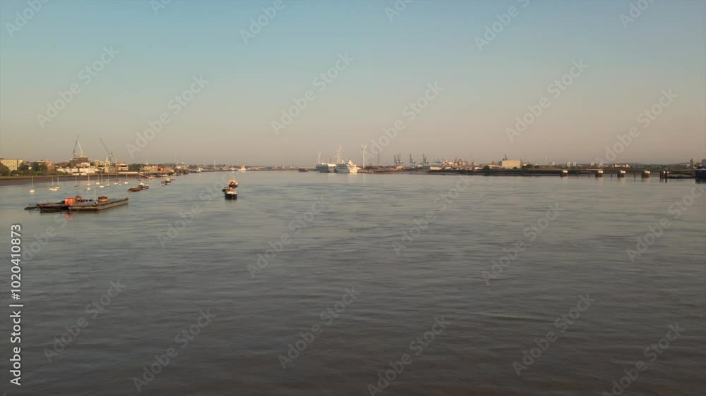Aerial view of the Thames River at sunrise, featuring barges and boats in the foreground with Tilbury Docks and wind turbines visible in the distance. Aerial view of the Thames River at sunrise, featuring barges and boats in the foreground with Tilbury Docks and wind turbines visible in the distance.