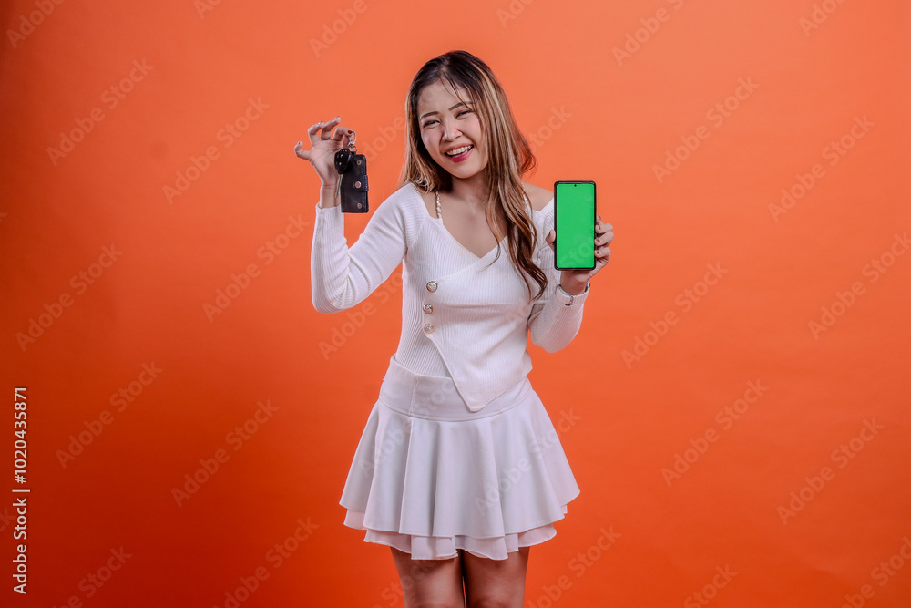 asian woman in white top standing very cheerful hand holding car key and mobile phone screen, gadget isolated orange background. for transportation, rental services, vehicle business, automotive asian woman in white top standing very cheerful hand holding car key and mobile phone screen, gadget isolated orange background. for transportation, rental services, vehicle business, automotive