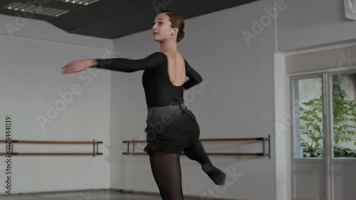 Medium shot of beautiful young Caucasian woman dressed in black leotards and tights performing elegant ballet pirouettes in spacious ballet class photo