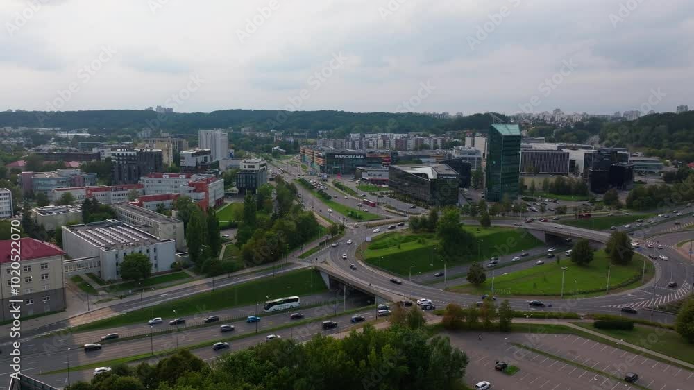 Aerial views capture cars navigating a highway interchange in Vilnius, Lithuania. Surrounding buildings and trees form an urban landscape beneath a cloudy sky Aerial views capture cars navigating a highway interchange in Vilnius, Lithuania. Surrounding buildings and trees form an urban landscape beneath a cloudy sky