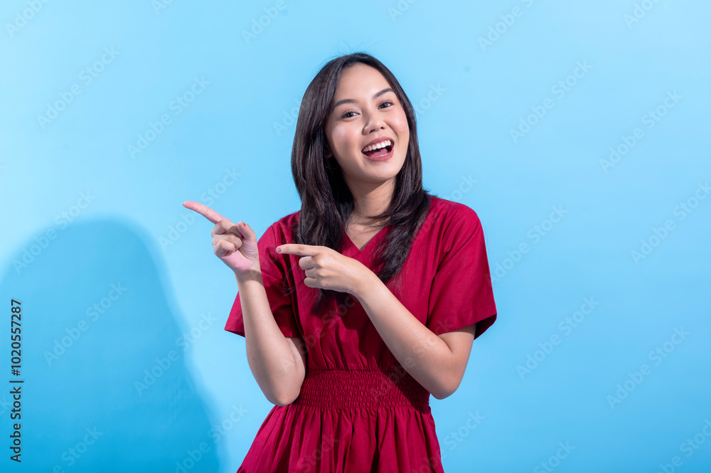 A young Asian woman wearing a red dress stands confidently against a light blue background, smiling and pointing with both hands. The playful gesture and vibrant colors create a cheerful A young Asian woman wearing a red dress stands confidently against a light blue background, smiling and pointing with both hands. The playful gesture and vibrant colors create a cheerful