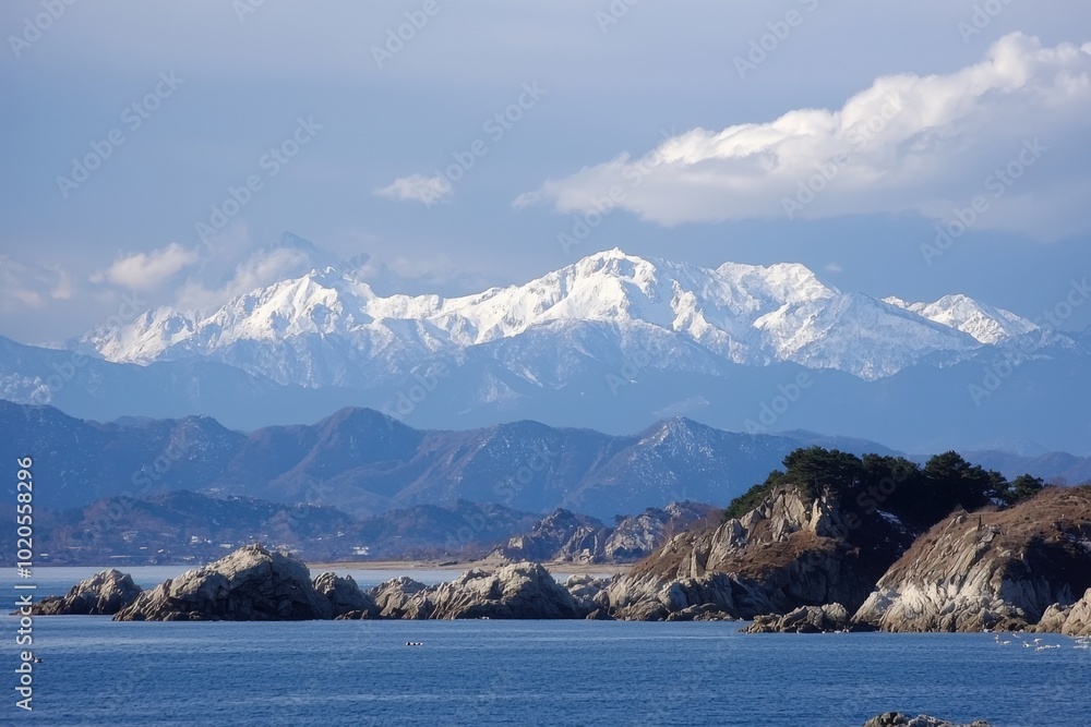 Snow-capped mountains loom majestically over a serene coastal landscape in winter sunlight Snow-capped mountains loom majestically over a serene coastal landscape in winter sunlight