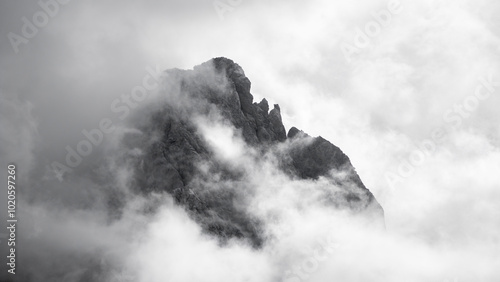 A dark, jagged mountain peak shrouded in thick clouds and mist. The scene is dramatic and atmospheric, with the mountain barely visible through the foggy cover, creating a sense of mystery