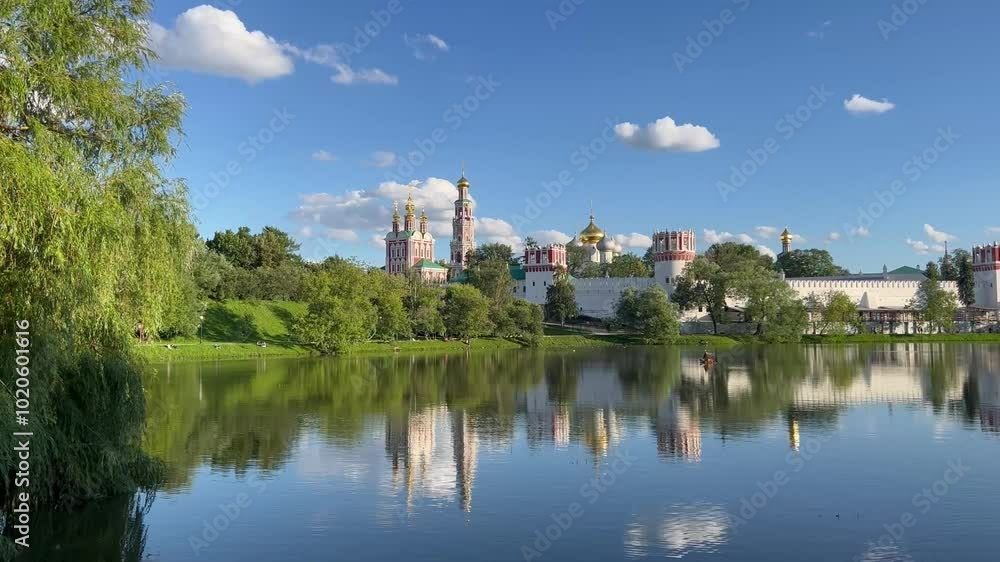 The towering spires of the Novodevichy Convent in Moscow, with its tranquil pond, lush gardens, and historic church buildings The towering spires of the Novodevichy Convent in Moscow, with its tranquil pond, lush gardens, and historic church buildings
