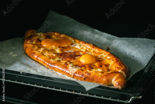 Close up view of ready-to-eat adjarian khachapuri with cheese and egg yolk. Freshly baked traditional Georgian cuisine with fluky crust in the oven photo