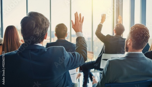 Young colleagues raising hands to ask questions during business meeting sitting back in office. Diverse business people voting at the conference in meeting room listening their