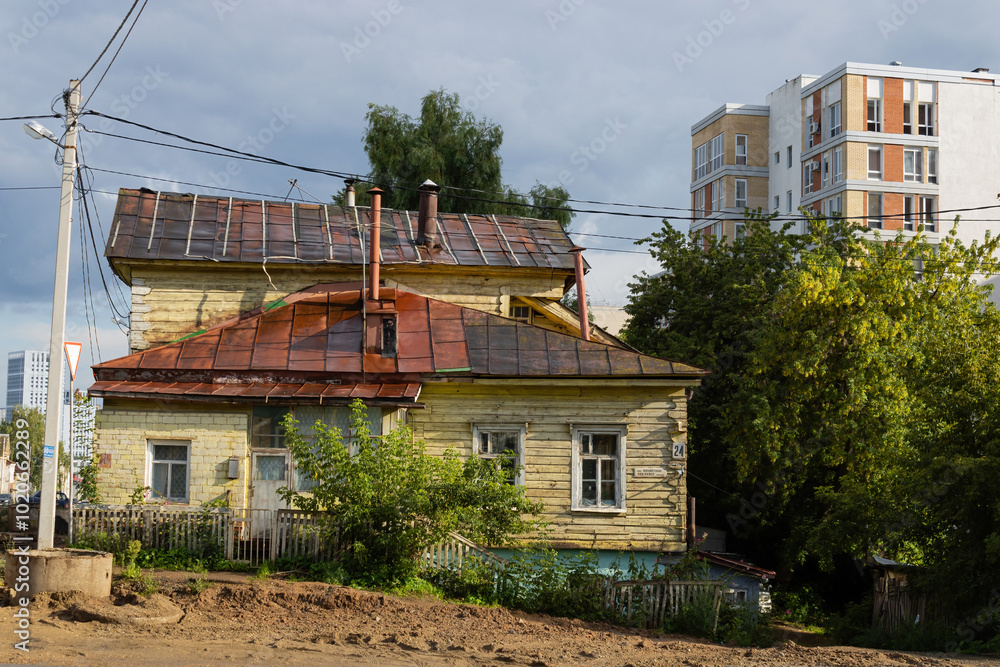 Old shabby house, dirty road. Pole and power lines. Modern high-rise buildings in the back. Eclectic architecture on the streets of Ufa. Bashkortostan Old shabby house, dirty road. Pole and power lines. Modern high-rise buildings in the back. Eclectic architecture on the streets of Ufa. Bashkortostan