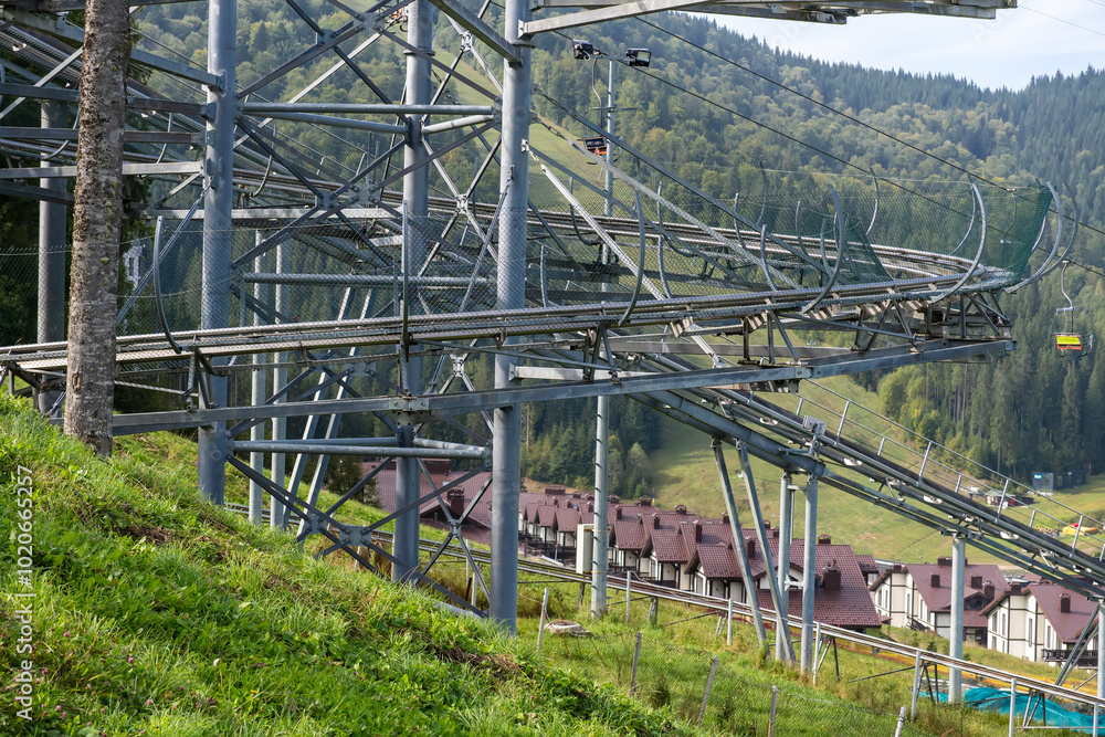 A summer toboggan run with many turns in the middle of a mountain forest with a view of the ski lifts. An attraction for an exciting descent with turns, bends and jumps. A summer toboggan run with many turns in the middle of a mountain forest with a view of the ski lifts. An attraction for an exciting descent with turns, bends and jumps.