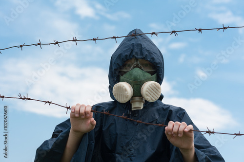 A man in a respirator and goggles looks like a stalker standing behind a barbed wire fence. photo