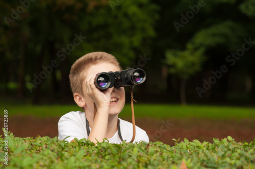 The boy with binoculars hiding behind the bushes and watches somebody