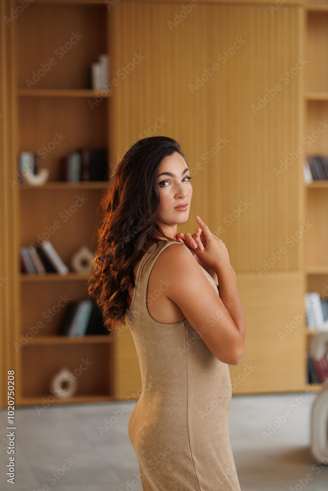 A beautiful tall brunette in a gold knitted dress. Spectacular volumetric styling. Beautiful rays of light. Portrait of a smile. The woman in front of the mirror A beautiful tall brunette in a gold knitted dress. Spectacular volumetric styling. Beautiful rays of light. Portrait of a smile. The woman in front of the mirror