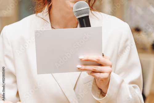 white blank paper card in hand of wedding or corporate presenter or event manager, young caucasian woman in white costume, mockup, copy space