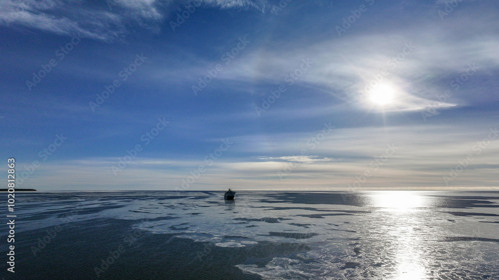 Cargo Ship Far Away in the Horizon on a Bright, Sunny, Clear Winter Day on a Calm, Dark Blue Semi-Frozen Sea