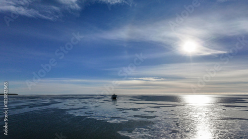 Obraz na płótnie Cargo Ship Far Away in the Horizon on a Bright, Sunny, Clear Winter Day on a Calm, Dark Blue Semi-Frozen Sea w salonie