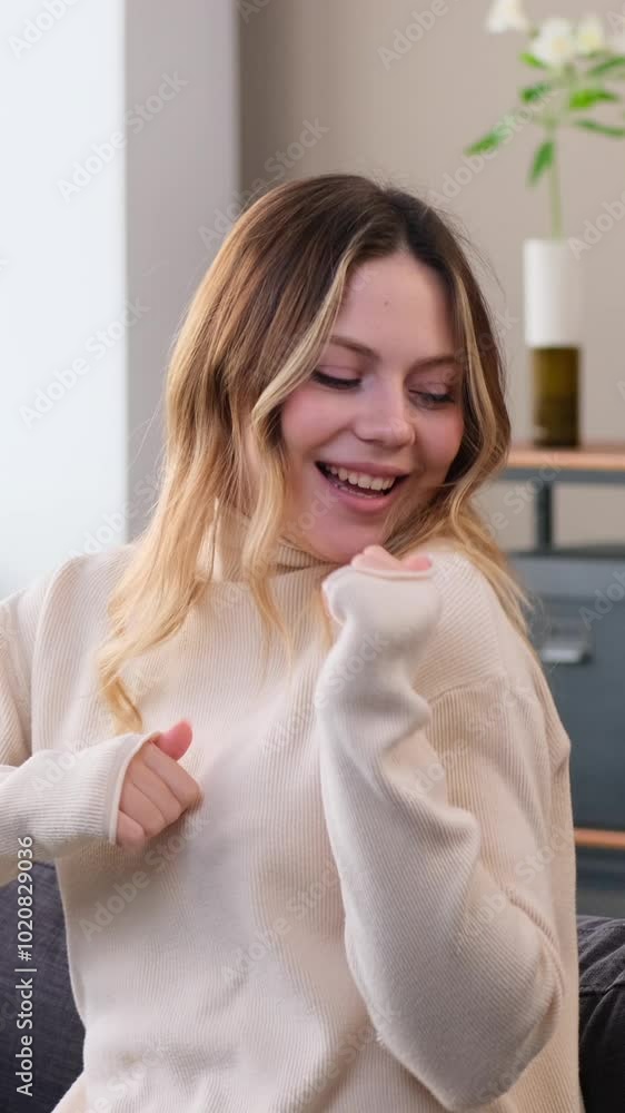 Happy Caucasian young adult woman dancing to music and having fun, spending leisure time on sofa at home. Concept of a pleasure and amusement. Vertical video. Happy Caucasian young adult woman dancing to music and having fun, spending leisure time on sofa at home. Concept of a pleasure and amusement. Vertical video.