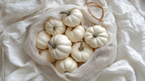 Little white pumpkins in a reusable cotton mesh bag on white linen fabric background Flat lay composition for eco friendly lifestyle and vegetable shopping concept