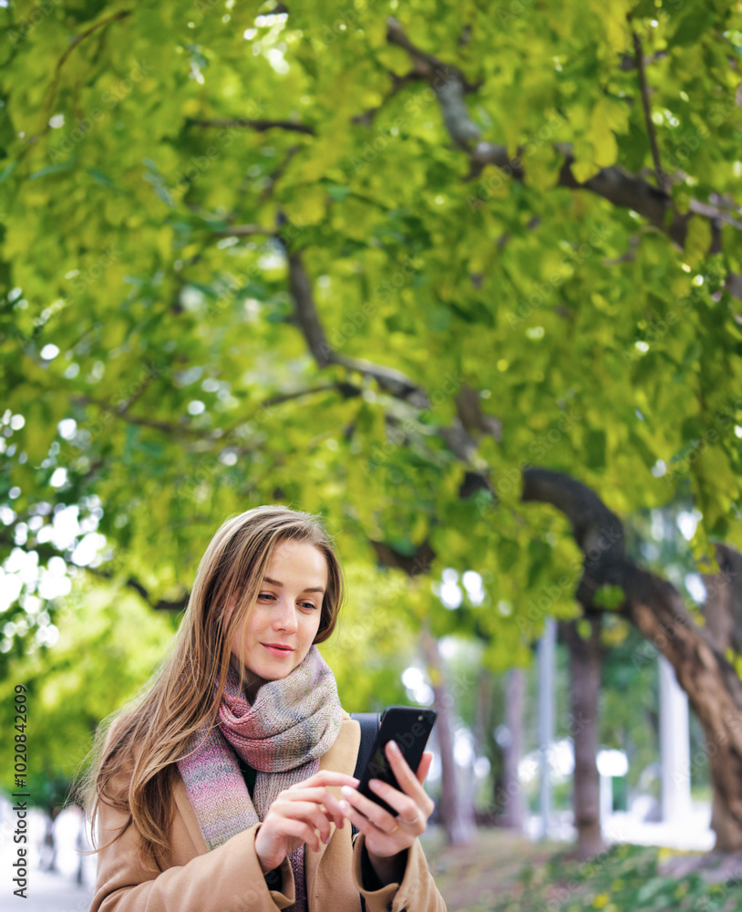 Young woman walking in a park with smartphone in her hands. Speaking on phone or sending messages outdoors Young woman walking in a park with smartphone in her hands. Speaking on phone or sending messages outdoors