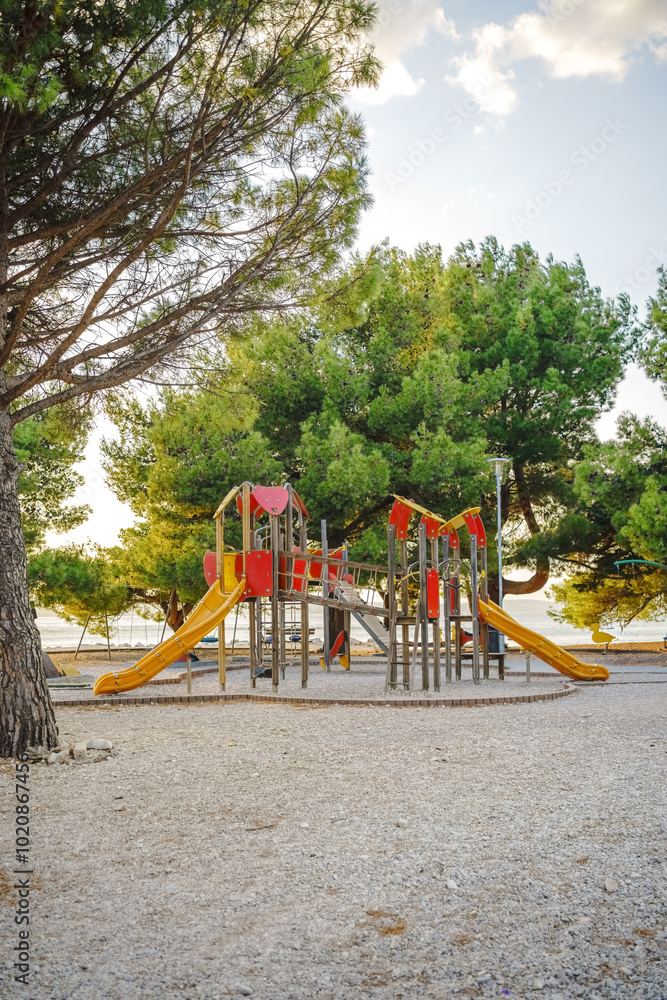 Vertical view of wooden playground in the beach between conifers tree at golden sunset 