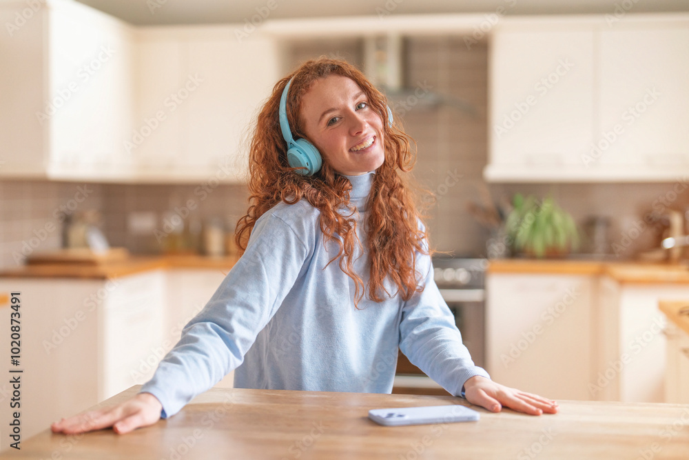 Joyful woman in blue sweater enjoying music while relaxing in a modern kitchen during a sunny morning Joyful woman in blue sweater enjoying music while relaxing in a modern kitchen during a sunny morning