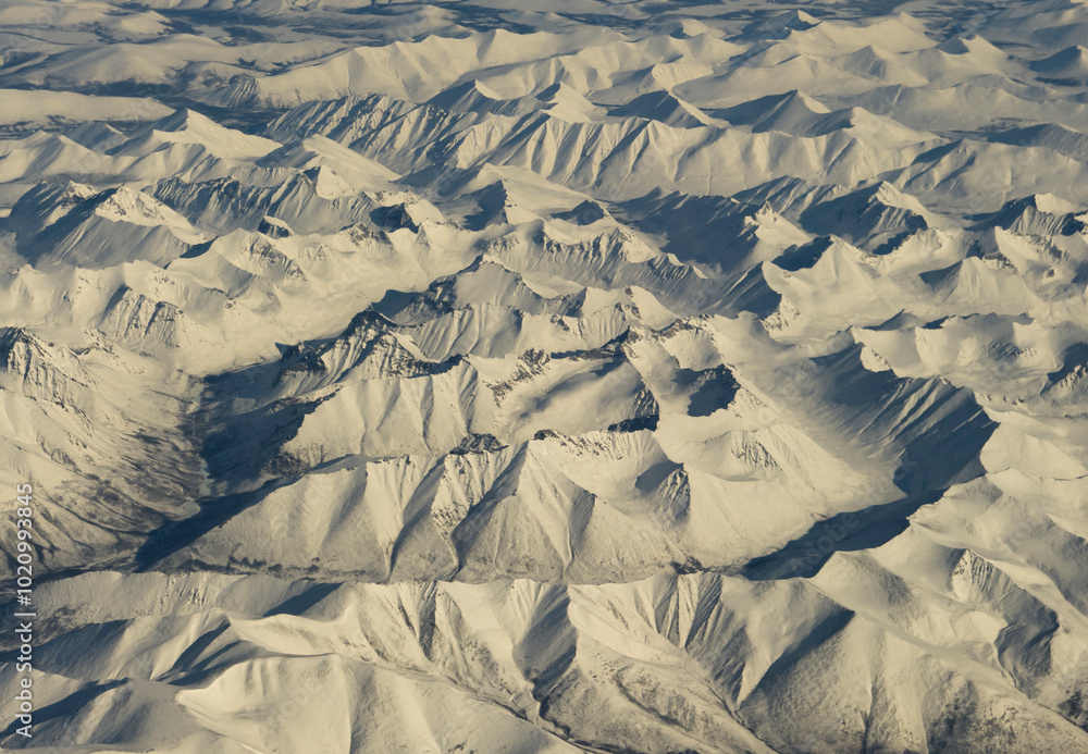 Fototapeta premium Russia. Eastern Siberia. View from the window of the plane to the snow-capped peaks of the mountains on the high plateau of the Irkutsk region.