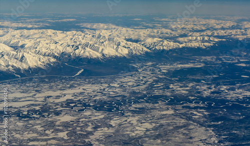 Russia. Eastern Siberia. View from the window of the plane to the snow-capped peaks of the mountains on the high plateau of the Irkutsk region.