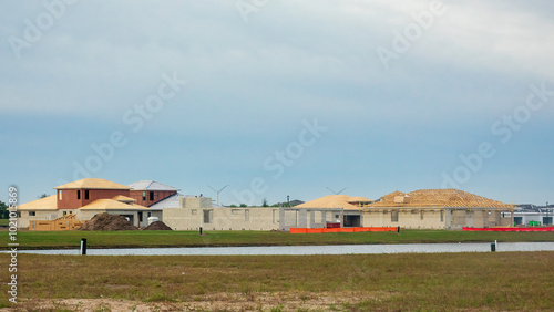 Single-family houses at various stages of construction near a pond in a suburban residential development on an overcast morning in southeast Florida, for motifs of building booms and population growth