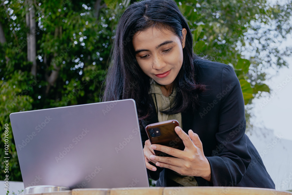 Businesswoman using mobile smart phone during working on laptop computer outdoors. Asian woman using smartphone searching the information with laptop, internet technology concept. Businesswoman using mobile smart phone during working on laptop computer outdoors. Asian woman using smartphone searching the information with laptop, internet technology concept.
