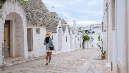 Fotografi Strolling through the picturesque, whitewashed streets of Alberobello Puglia, a traveler admires the iconic trulli architecture under a softly lit sky