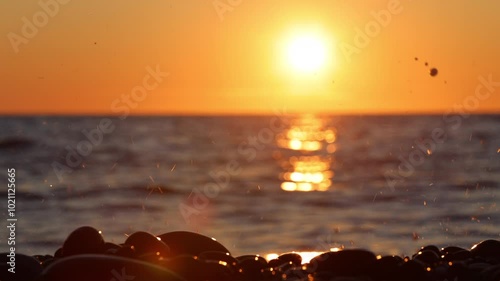 sea ​​waves crash against rocks and spray forms in the setting sun