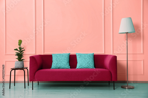Εκτύπωση καμβά Stylish sofa with cushions, floor lamp and side table with plant near wall