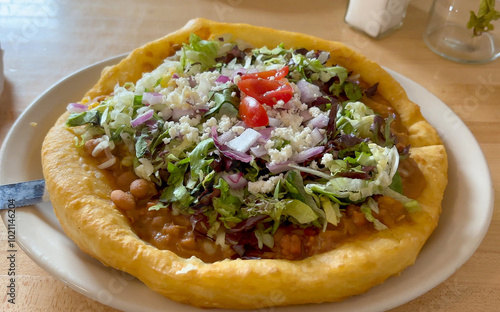 Close-up shot of a Navajo Taco, a traditional Native American frybread topped with beans, lettuce, tomatoes, cheese, and onions, served in an Arizona restaurant. Fresh and tasty ingredients - USA