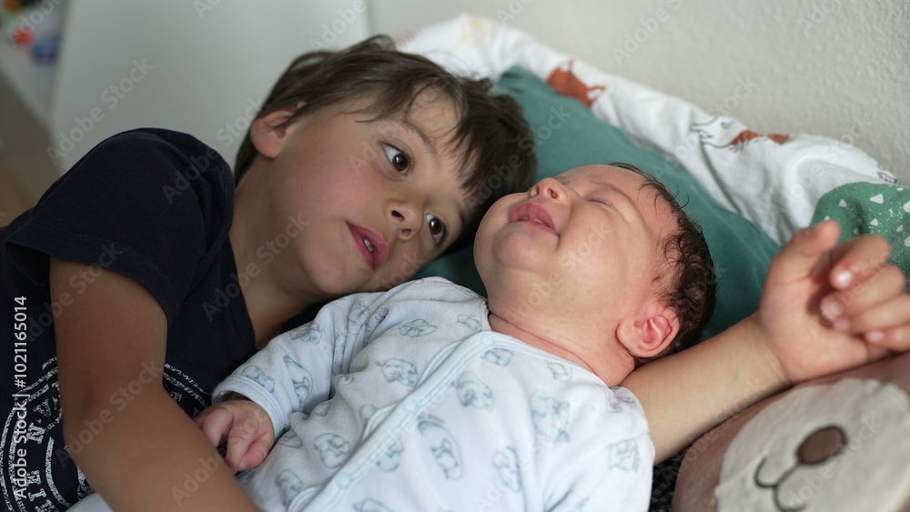 Big brother lying next to his newborn sibling, gazing affectionately at the baby, both cuddling on a bed with soft blankets, home environment, nurturing family moment captured Big brother lying next to his newborn sibling, gazing affectionately at the baby, both cuddling on a bed with soft blankets, home environment, nurturing family moment captured