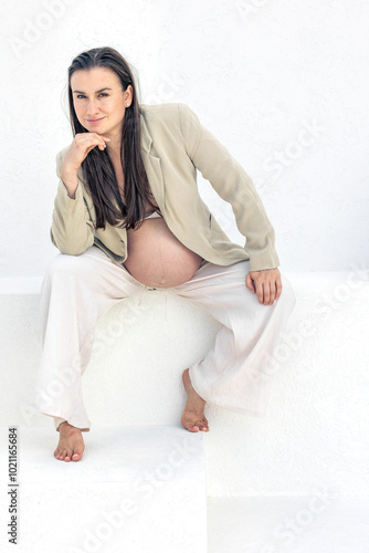 Stylish pregnant woman in a suit on a light background. Pregnancy concept.