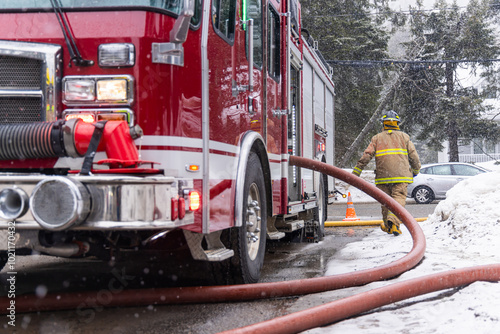 Fotomural Fireman is walking through the snow pulling a large fire hose away from the firetruck during a snowstorm