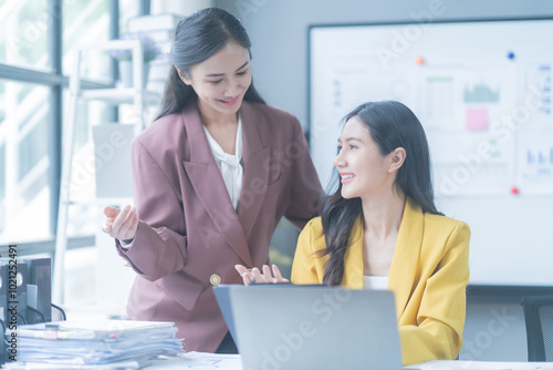 Two businesswomen collaborating on laptop in modern office, strategizing and analyzing charts, showcasing teamwork and professionalism in bright, airy space photo