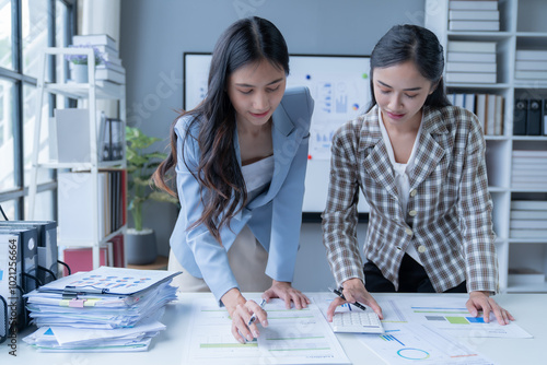 Two businesswomen collaborating in an office, analyzing financial documents and strategizing for success. Focused on teamwork, problem-solving, and effective communication photo