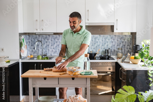 Happy man cutting bread in kitchen enjoying weekend at home