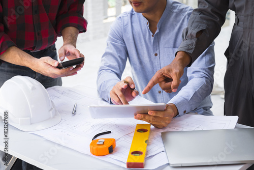 Engineers and architects pointing at digital tablet screens. Two Construction Engineers or Architects discussing at work with digital tablet, laptop and blueprint on construction site.