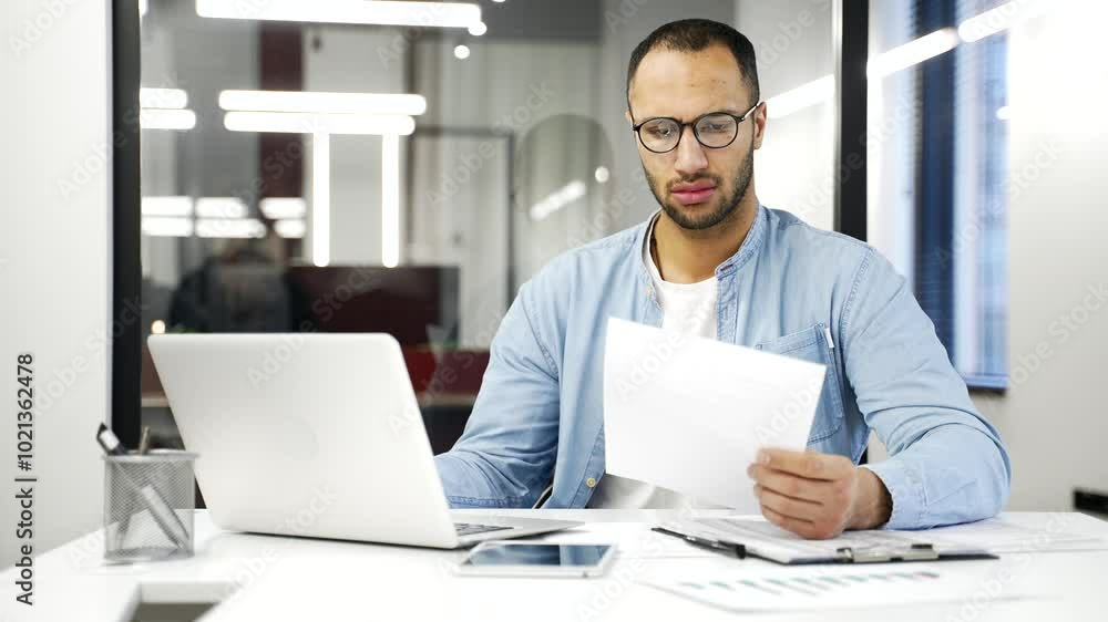 Frustrated african american financier unhappy with bad financial results checking documents on laptop . Confused puzzled black man employee having difficulty with paper work sitting in business office Frustrated african american financier unhappy with bad financial results checking documents on laptop . Confused puzzled black man employee having difficulty with paper work sitting in business office