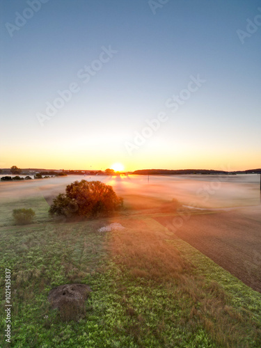 Sonnenaufgang über Schweinfurt mit Nebelschleiern, Nebel über den Feldern, mit einem Bach und Bäumen und die aufgehende Sonne am Horizont, Drohnenfoto, Luftaufnahme, Schweinfurt, Bayern, Deutschland	
 photo