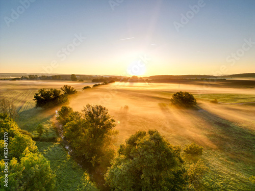 Sonnenaufgang über Schweinfurt mit Nebelschleiern, Nebel über den Feldern, mit einem Bach und Bäumen und die aufgehende Sonne am Horizont, Drohnenfoto, Luftaufnahme, Schweinfurt, Bayern, Deutschland	
