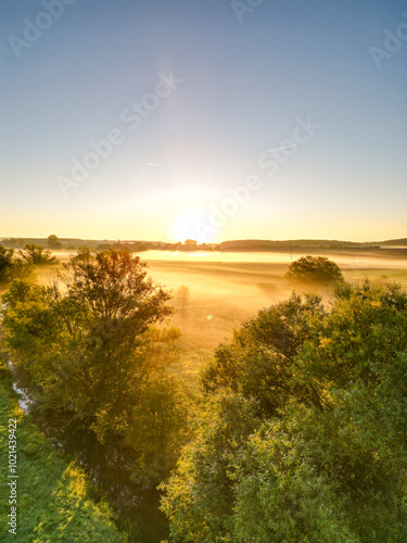 Sonnenaufgang über Schweinfurt mit Nebelschleiern, Nebel über den Feldern, mit einem Bach und Bäumen und die aufgehende Sonne am Horizont, Drohnenfoto, Luftaufnahme, Schweinfurt, Bayern, Deutschland	
 photo