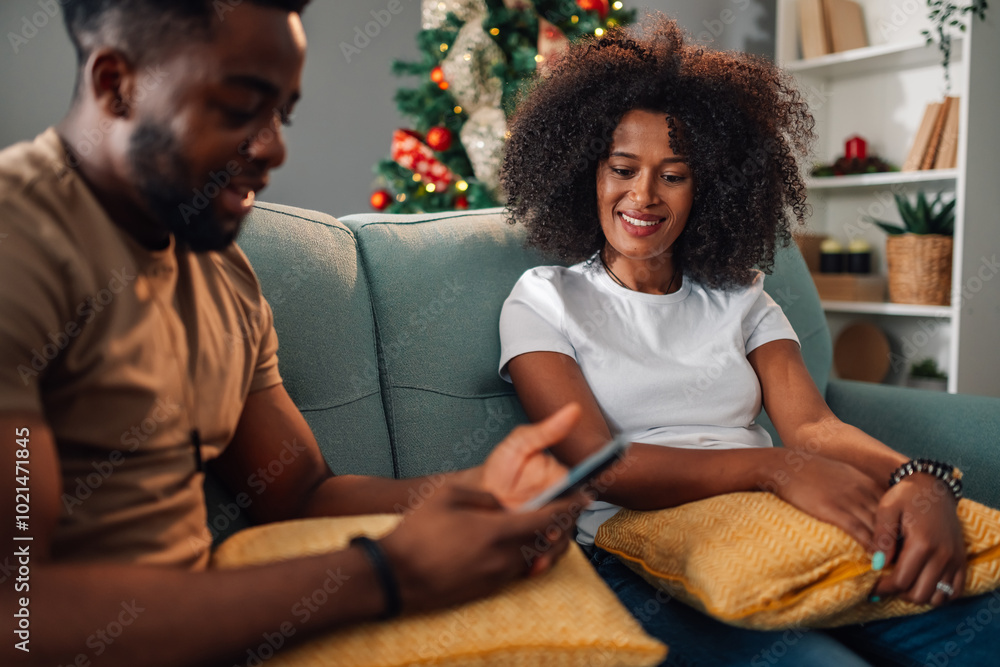 Diverse couple share a digital moment on the sofa during the holidays Diverse couple share a digital moment on the sofa during the holidays