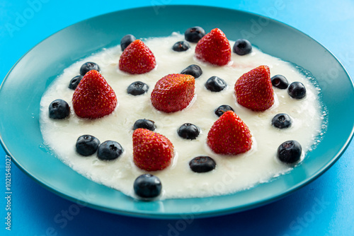 Fresh juicy berries strawberries and blueberries in a blue plate with whipped cream on a blue background