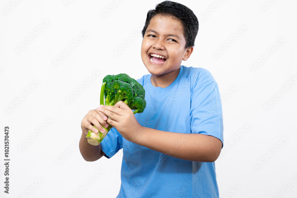 Cute and active Indonesian boy standing while posing to use broccoli vegetables, concept of healthy lifestyle, healthy and nutritious vegetables, isolated white background.
